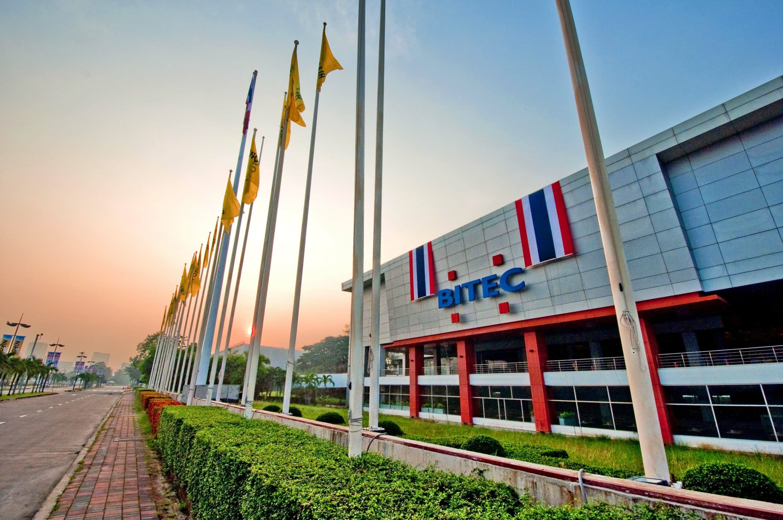 BITEC building with Thai flag colors and a row of tall yellow flags at sunset.