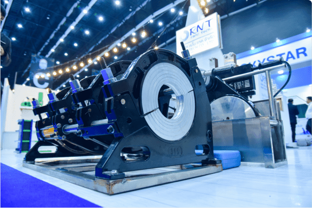 Heavy-duty pipe welding machine with circular metal clamps displayed at an industrial trade show.